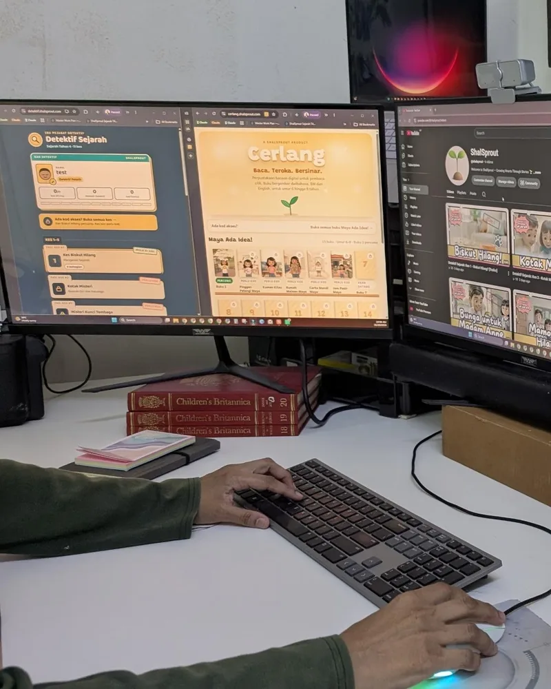Tangan Shaliza di meja kerja, dengan Detektif Sejarah, Cerlang dan saluran YouTube ShalSprout di skrin.